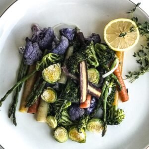 roasted vegetables on a plate with a lemon and a sprig of thyme.