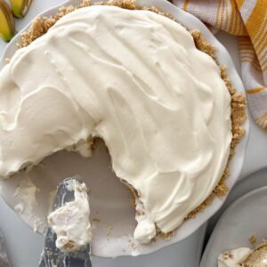 pie with a whipped cream top, about a quarter of the pie cut out. Surrounded by a napkin and a pie server.