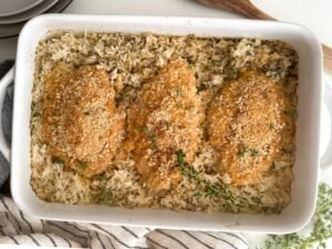 three cooked chicken breasts on rice in a casserole dish