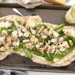 pizza on a baking sheet with ceasar salad dressing on the side.