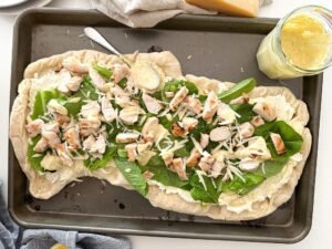 pizza on a baking sheet with ceasar salad dressing on the side.