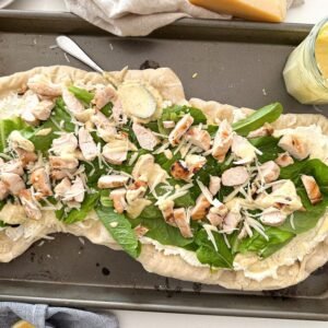 pizza on a baking sheet with ceasar salad dressing on the side.