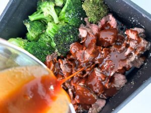 Pouring sauce over the crispy beef and broccoli.