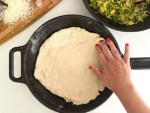 In the cast iron pan, sprinkle the bottom with the corn meal and press out the pizza dough.