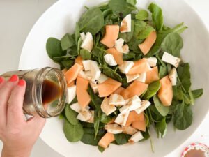 Pouring the Honey Balsamic Vinaigrette onto the spinach and melon salad.