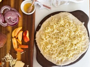 Laying on shredded fontina cheese for the peach prosciutto pizza