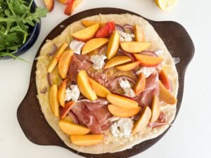 Add the ripe peaches to the pizza, between the goat cheese and prosciutto.