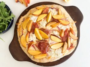 Pizza fresh out of the oven. Creamy melted cheese with oven roasted peaches and crispy prosciutto.